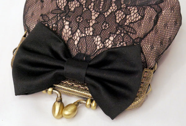 Small purse made of blush satin with a black lace overlay, black satin bow and antique brass frame.