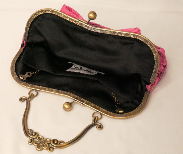 black sequin handbag with a pink lace overlay and pink bow, attached to an antique brass frame with a handle