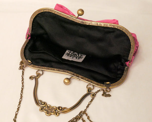 black sequin handbag with a pink lace overlay and pink bow, attached to an antique brass frame with a handle