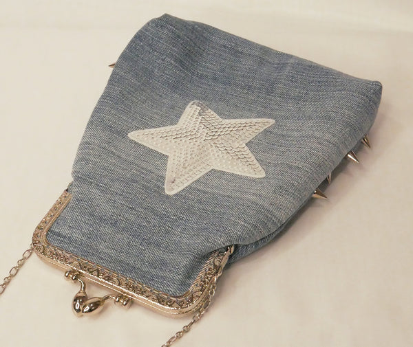 Blue denim handbag with silver studs and a silver star patch, with pink satin lining and a silver metal frame and chain wrist strap